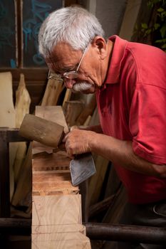 Old woodcarver working with mallet