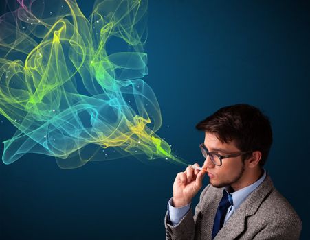 Handsome young man smoking cigarette with colorful smoke