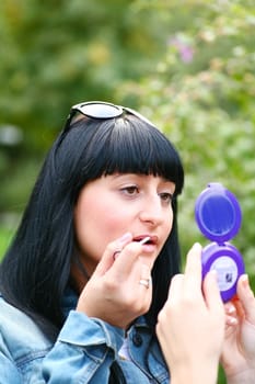 A young woman applying makeup on her lips