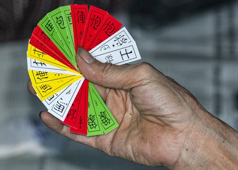 White, yellow, green and red Chinese cards in dirty worker's hand.