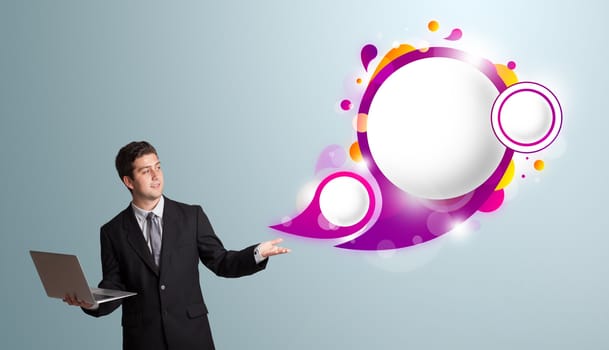 Attractive young man holding a laptop and presenting abstract speech bubble copy space 
