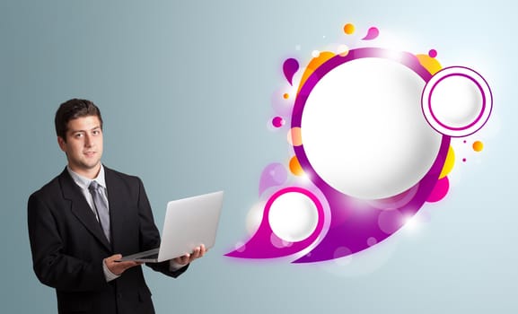 Attractive young man holding a laptop and presenting abstract speech bubble copy space 