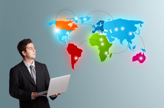 Handsome young man holding a laptop and presenting colorful world map