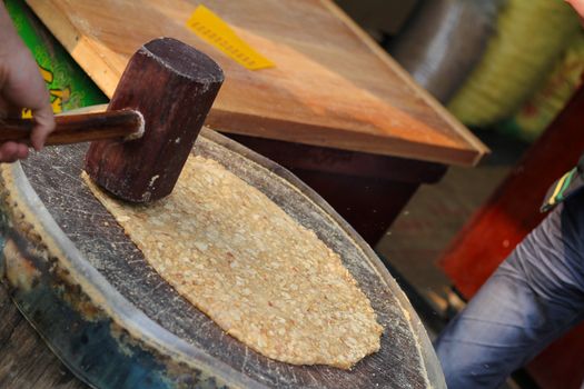Traditional Chinese almond candy being prepared using wooden hammer on tree stump
