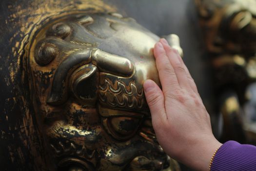 Hand touching bronze lion head, in the Forbidden city, Beijing
