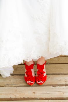 A bride wearing her beautiful red wedding shoes on her wedding day. They are stilettos of vibrant color.
