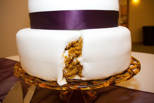 A cake with a big slice taken out by the bride and groom after they cut the cake.
