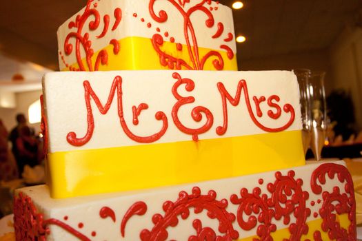 A wedding cake that says mr and mrs on it in red writing at a wedding reception indoors.