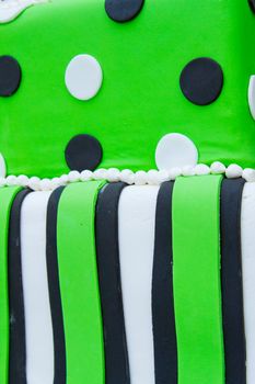 A very non-traditional wedding cake with white, green, and black and polkadots on it at the reception for a bride and groom.