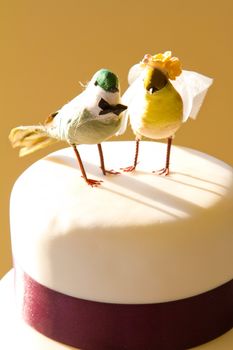 A traditional white wedding cake is topped with craft birds and wrapped in purple ribbon at the bride and groom's reception.