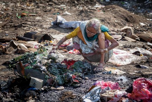 Pollution and poverty : Indian old female sitting  for warmup  herself near fire  in  garbage,