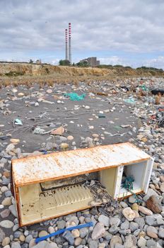 Trashed fridge on the seashore next to a factory