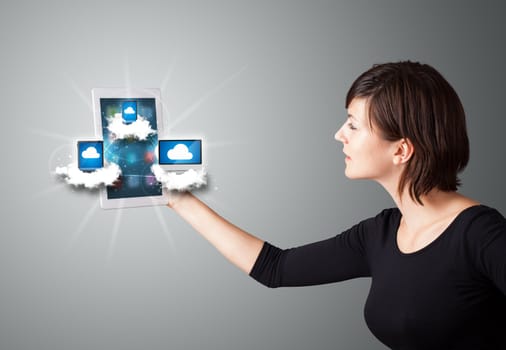 Beautiful young woman holding tablet with modern devices in clouds