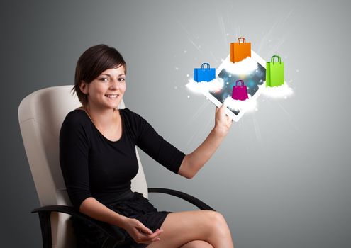 beautiful woman holding modern tablet with colorful shopping bags on clouds