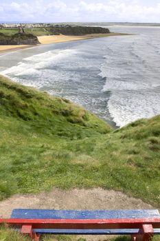 a scenic view of Ballybunion castle and beach on a bright sunset evening from a bench