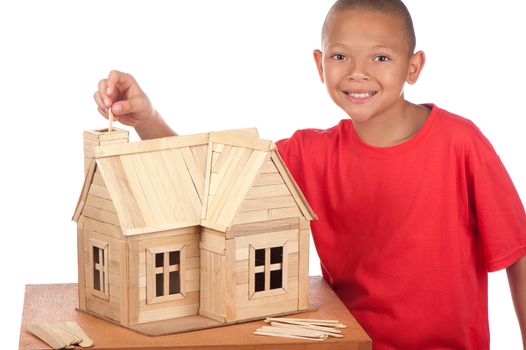 A smiling young boy stands next to the popsicle house he is building.