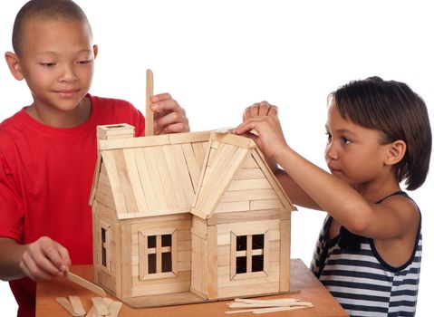 A young girl and boy enjoy building a wooden toy house together.