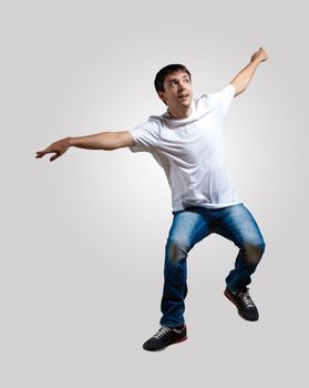 Modern slim hip-hop style man jumping dancing on a grey background