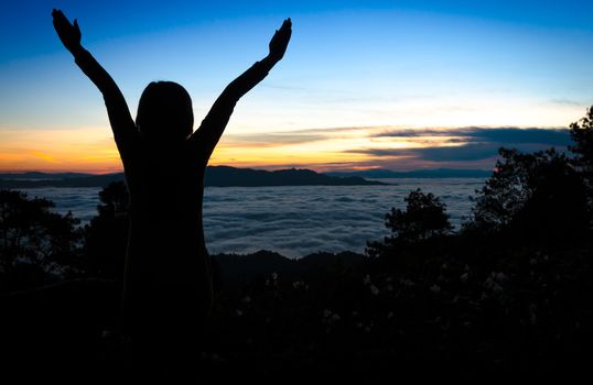 Silhouette of happy woman with hands up enjoying over sunset