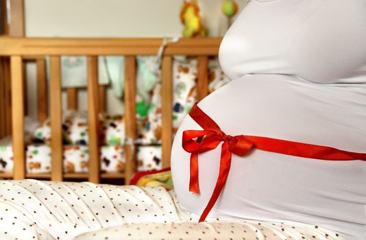 Pregnant woman tummy decorated with red ribbon and bow 