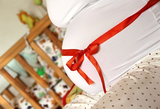 Pregnant woman tummy decorated with red ribbon and bow 