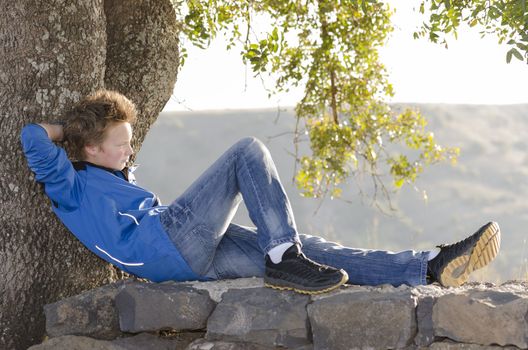 Teenager sitting on a rock under a tree