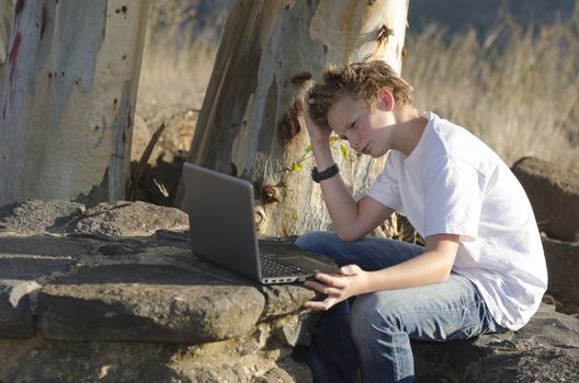 Thoughtful teenager sits on nature with laptop