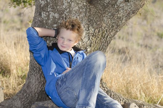 Teenager in sportswears sits under tree on nature