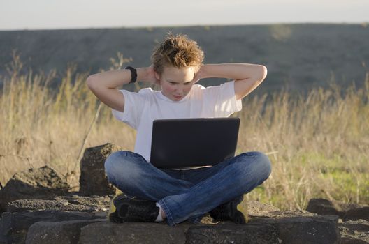 Resting teen with mobile computer hold hands behind his head in nature at sunset
