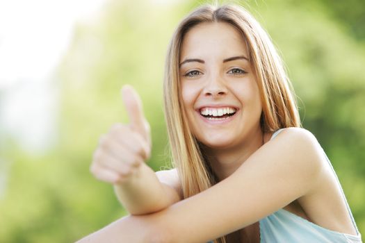 Young smiling blond female outdoors showing thumb up sign