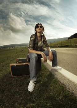 Girl in the road sit atop vintage suitcase