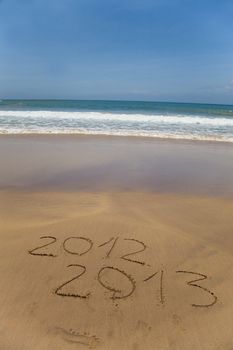 2012 and 2013 written in sand on beach with sea waves starting to erase the word 