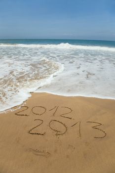 2012 and 2013 written in sand on beach with sea waves starting to erase the word 