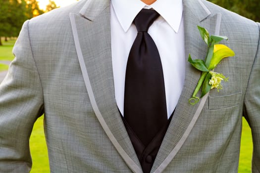 A groom and his boutonniere on his wedding day. He is wearing a suit with a single flower on the lapel of his jacket.