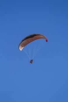 A paraglider takes to the sky. Shot from below against a blue sky.