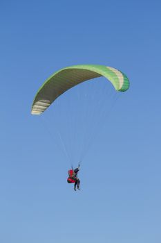 A paraglider takes to the sky. Shot from below against a blue sky.