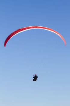 A paraglider takes to the sky. Shot from below against a blue sky.