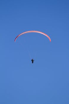 A paraglider takes to the sky. Shot from below against a blue sky.