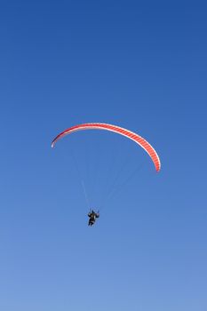 A paraglider takes to the sky. Shot from below against a blue sky.