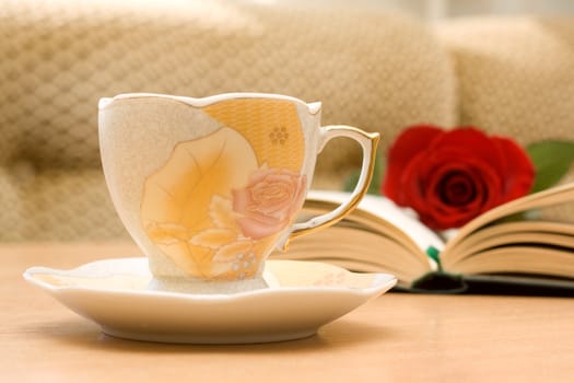 Cup of tea and an open book on the table with a rose