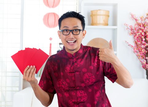 Thumb up Asian Chinese man showing many red packets / ang pow , indoors