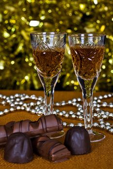 Crystal glasses of brandy and chocolate on the background of holiday lights.