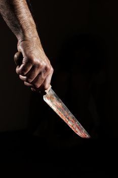 Man with bloody knife, hand close up, dark background