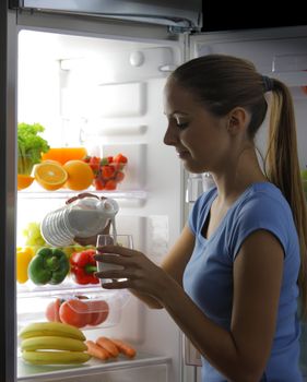 Young woman  pour out milk into glass near refrigerator at night