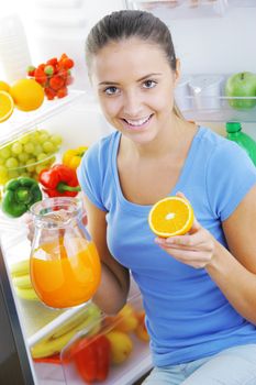 Beautiful young woman near refrigerator with a carafe of orange juice