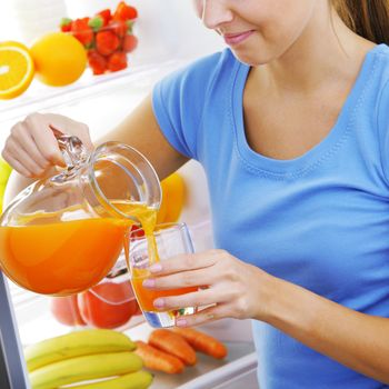 young woman near a refrigerator pouring orange juice, hands close up