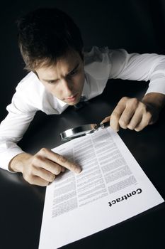 Young businessman looking to a contract through a magnifying glass 