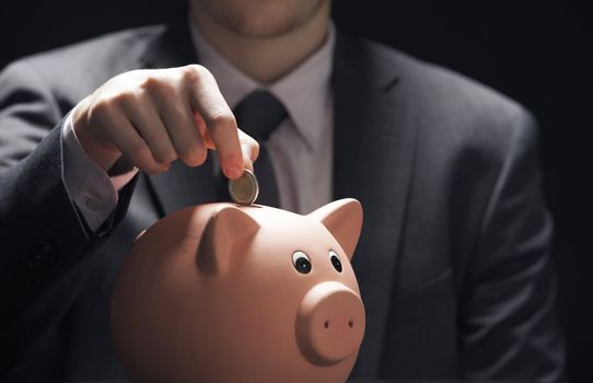 Businessman hand putting coin into a piggy bank