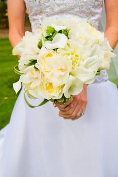 A bride in beautiful white wedding dress holds a bouquet of white and green flowers.