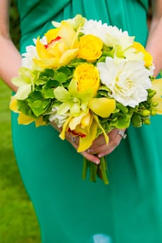 A bridesmaid in a teal green dress holds a bouquet of flowers during a wedding.